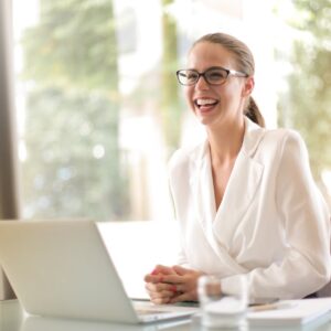 Cheerful businesswoman in glasses working on a laptop, in a bright and modern office setting.