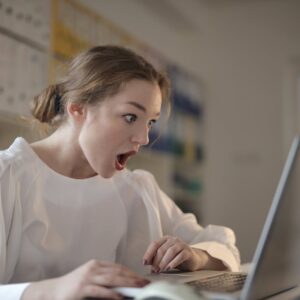 Surprised woman sitting at desk with laptop indoors, expressing amazement.