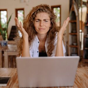 A woman frustrated with her laptop while working remotely indoors, expressing stress.