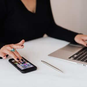 A professional woman multitasking with a smartphone and laptop at an office desk.
