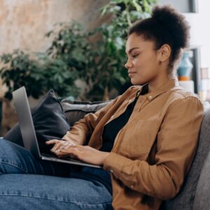A young woman in casual clothing works on her laptop in a cozy home office setting.